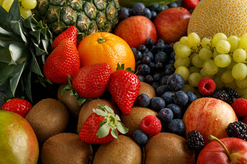 Variety of fresh fruits and berries on dark background: cantaloupe, melon, watermelon, blueberry, oranges, apple, strawberry, pineapple, mango, grapes and kiwi.