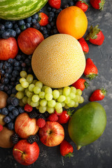 Variety of fresh fruits and berries on dark background: cantaloupe, melon, watermelon, blueberry, oranges, apple, strawberry, pineapple, mango, grapes and kiwi.