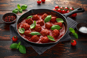 Homemade Meatballs in iron cast with sweet and hot tomato sauce, basil. On wooden table