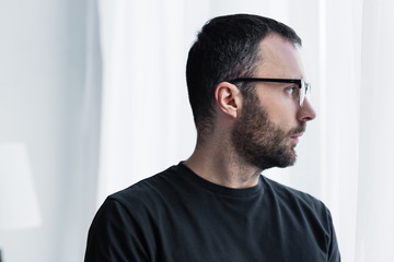 Obraz premium handsome pensive man in glasses looking out window at home
