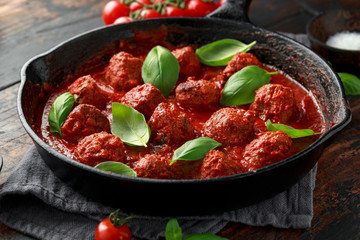 Homemade Meatballs in iron cast with sweet and hot tomato sauce, basil. On wooden table