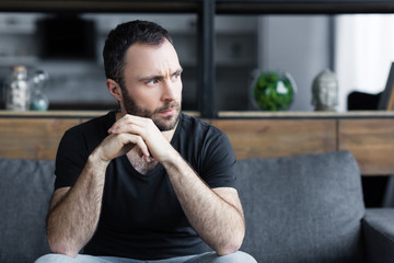 serious bearded man sitting on sofa with folded hands and looking away
