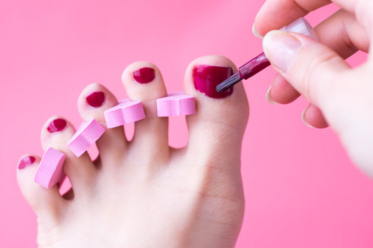 Woman foot pedicure at home with nail separators and red nail polish on pink background