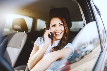 Fototapeta na wymiar Beautiful smiling brunette dressed elegant talking on the phone while driving her car.