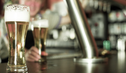 glass of beer on bar counter against background of friendly bartender