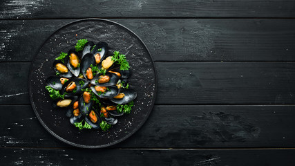 Boiled mussels with parsley and spices on a black plate. Top view. Free space for your text.