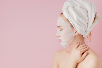 Beautiful young woman is applying a cosmetic tissue mask on a face on a pink background. Healthcare...