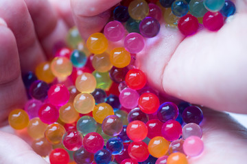 The child is holding multicolored plastic gel balls.