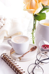 Morning coffee mug with glasses on a notebook, candle and rose on a white bed top view . Woman cozy morning