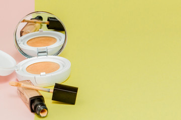 Make up products spilling on to a bright yellow and pink background with copy space