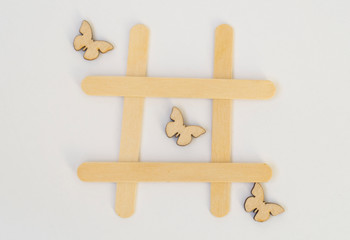 Three wooden butterflies lie in a row in the game of tic-tac-toe, in a grid on a white background. Concept summer