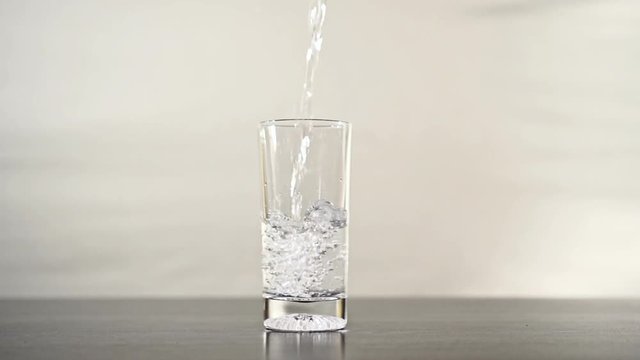 Pouring water into a glass until it overflowsPouring glass of water in slow motion until it overflows. Overfilling the liquid until the water flows onto the table.