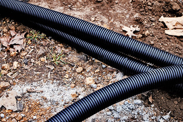 Fragments of three long black corrugated tubes are lying on the ground in the park to make a...
