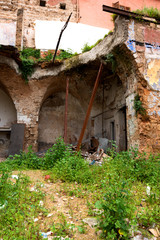 Abandoned ruined house near residential building. Broken stone wall and arches supported by rusty metal props. Collapse danger concepts. Safety problem background. 