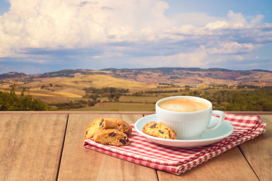 Coffee cup with biskotti cookies on wooden table over Tuscany landscape background