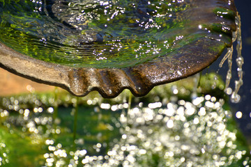 stone water bowl of a fountain close up view with light and bokeh visual background, water drops in the fountain macro shot with algae on the ground with bokeh effects