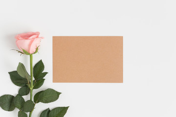 Top view of a kraft card mockup with a pink rose on a white table.