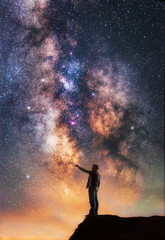 Naklejka na ściany i meble Man standing on the cliff and touching the milky way galaxy