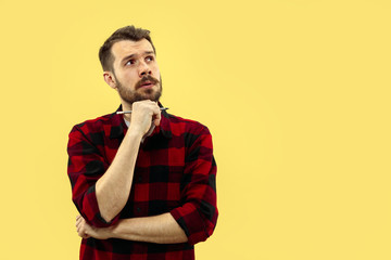 Half-length close up portrait of young man in shirt on yellow background. The human emotions, facial expression concept. Front view. Trendy colors. Negative space. Thoughtful, thinking.