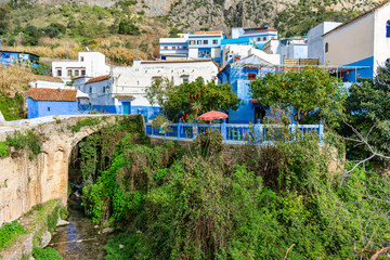 Patio with Red Umbrella beside a Stream with Blue and White Colored Homes and Buildings in Chefchaouen Morocco	