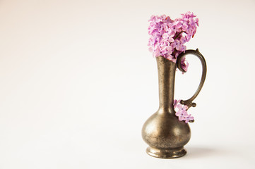 iron vase with lilac flowers stands on the table on a white background
