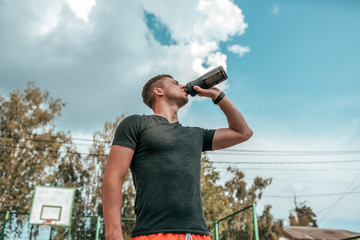 Male athlete, drinking water and protein from shaker, fitness watch, training in the city in the fresh air. Concept morning run in the city, fitness and workout, smart watch bracelet. Sportswear T