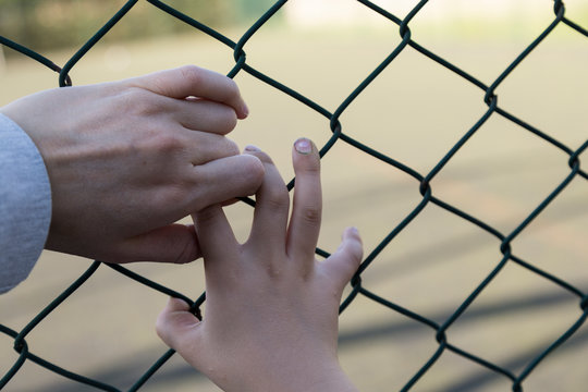 the girl hold the stadium iron wire mesh and look at the playing people.