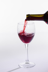 Pouring red wine into the glass on white background