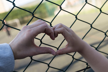 the girl hold the stadium iron wire mesh and look at the playing people.