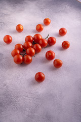 Bunch of cherry tomatoes on white textured stone concrete table, side view with copy space. Ingredients for cooking.