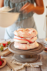 Process of decorating meringue cake with whipped cream and fresh strawberry