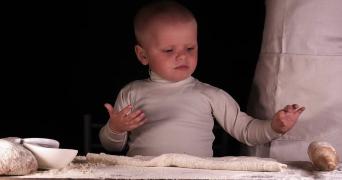 A little boy on a black background helps his father (dad) chef, preparing the dough to roll out for the pizza buns bread cakes and various flour products. Concept of: Little Chef, Baker, Slow motion.
