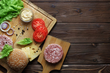 Raw ingredients for delicious home-made burger with copy space on dark wooden table