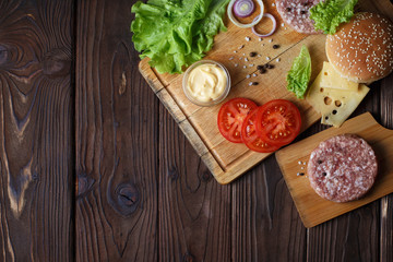 Raw ingredients for delicious home-made burger with copy space on dark wooden table