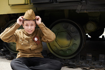 Fototapeta na wymiar Boy dressed in Soviet military uniform during the second world war posing near army tank
