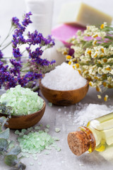 Sea salt in bowl, aroma oil in bottles, Wellness and flowers on grey textured background and flowers on vintage wooden background. Selective focus.