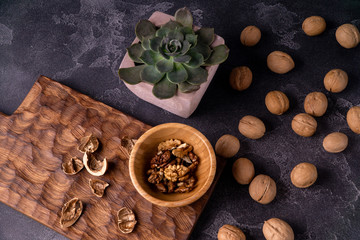 Walnut kernels in wooden bowl, whole walnuts and Echeveria plant on blue slate table. Healthy nuts and seeds composition.