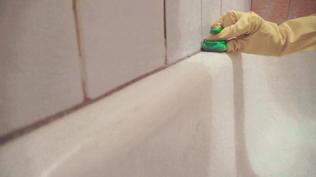 A woman doing things in the bathroom, removes the shower shelf. A woman rubs a bath and brushes walls and tiles with a brush and cleaning agent.