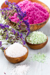 Sea salt in bowl, aroma oil in bottles, Wellness and flowers on grey textured background and flowers on vintage wooden background. Selective focus.