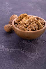 Cracked and whole walnuts in wooden bowl and on blue slate surface. Healthy nuts and seeds composition.