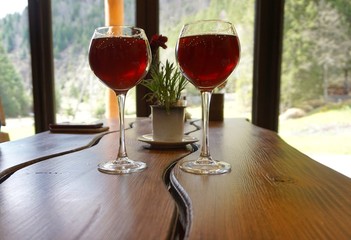 Two gTwo glasses of wine on the table. In the background is a window overlooking the mountains.lasses of wine on the table. In the background is a window overlooking the mountains.