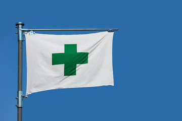A green cross sign, safety first aid flag on blue sky background.
