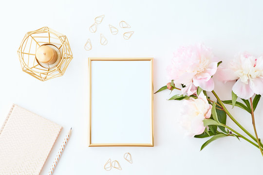 Flat lay composition with golden frame and light pink peonies on a white background