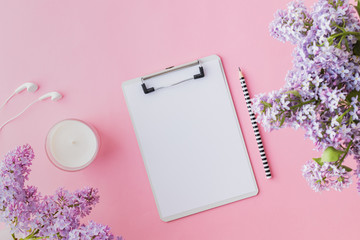 Flat lay blogger or freelancer workspace with a mockup clipboard and branches of lilac on a pink background