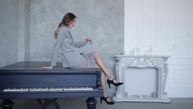 Sexy girl sitting on piano in striped suit and stroking her legs