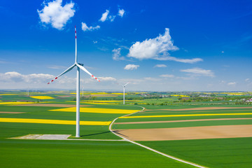 Aerial view of wind turbine. Rapeseed blooming. Windmills and yellow fields from above....