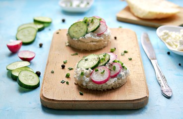 White bread sandwiches with salted cottage cheese, fresh radish and cucumber on a light blue background. Healthy food.