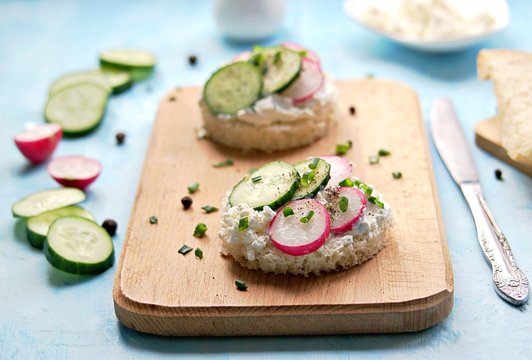 White bread sandwiches with salted cottage cheese, fresh radish and cucumber on a light blue background. Healthy food.