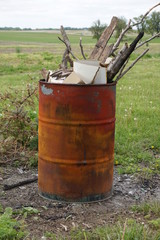 Obraz premium A rusted burn barrel overflowing with sticks and trash.