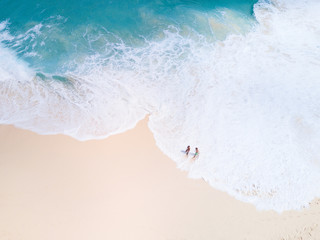 Top view from aerial. Bali drone shoot with ocean waves and white sand. People walk